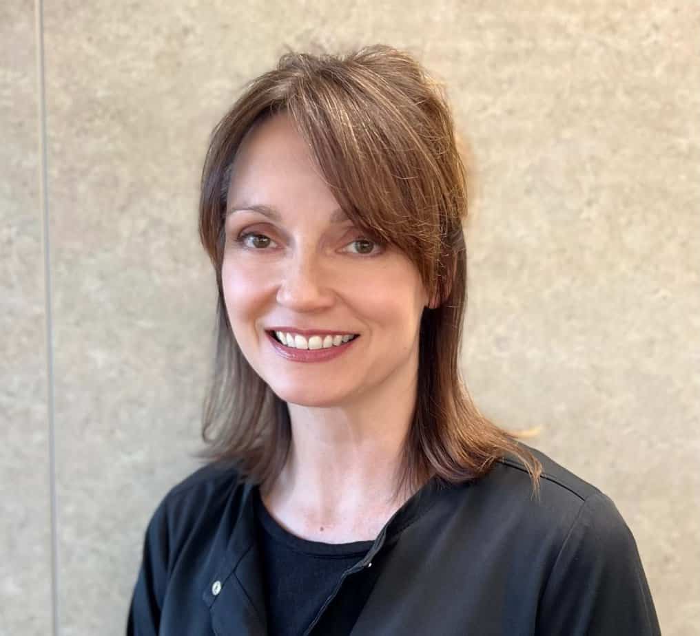 Tiffany, a woman in a black shirt, smiling in front of a wall.