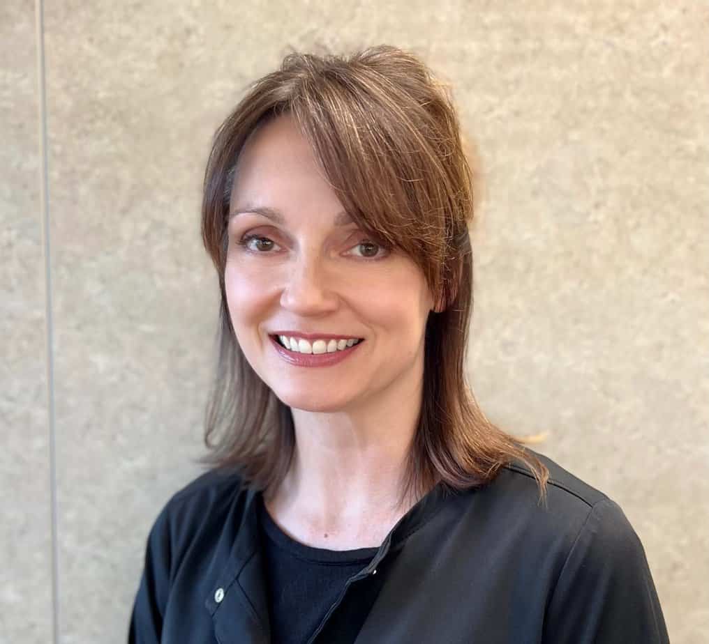 Tiffany, a woman in a black shirt, smiling in front of a wall.