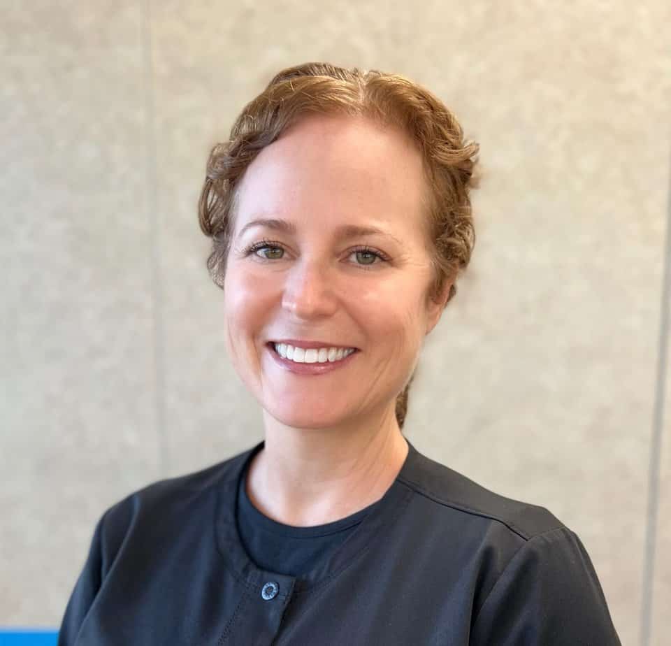 Melissa, a smiling woman, stands confidently in front of a black wall.