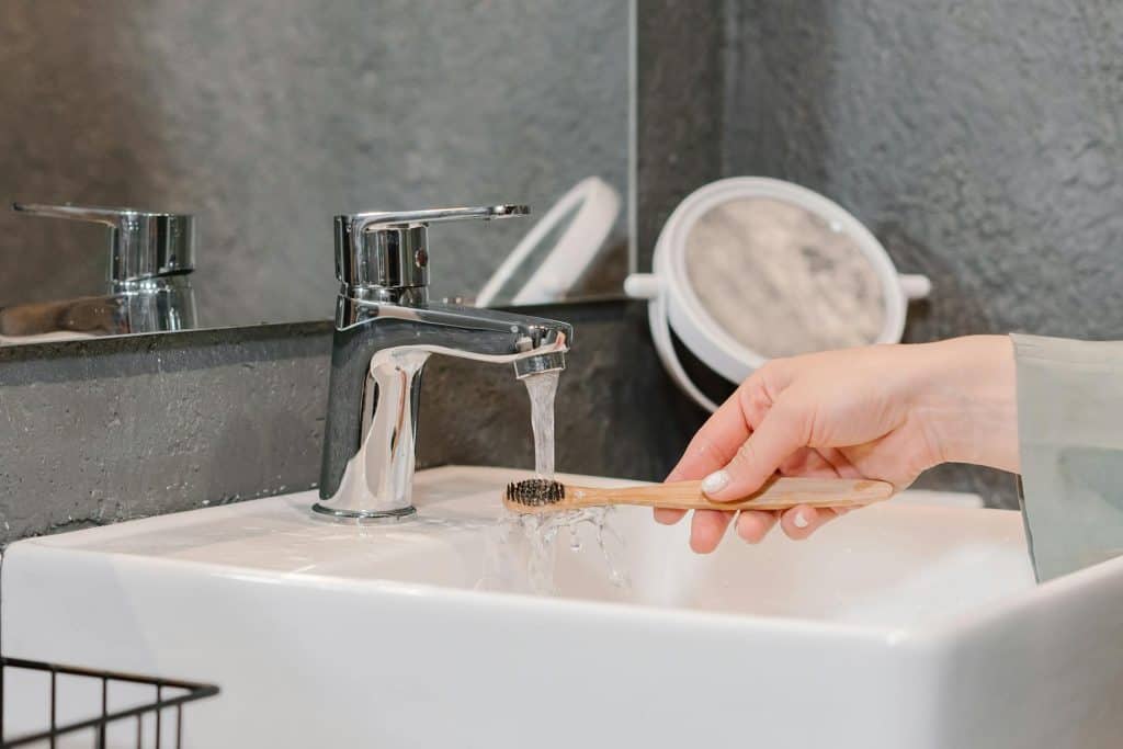 A woman is washing her face with a toothbrush in a sink, using cosmetic teeth fillings.