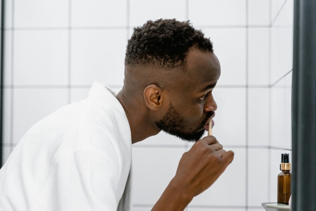 A man is whitening his teeth in front of a mirror.
