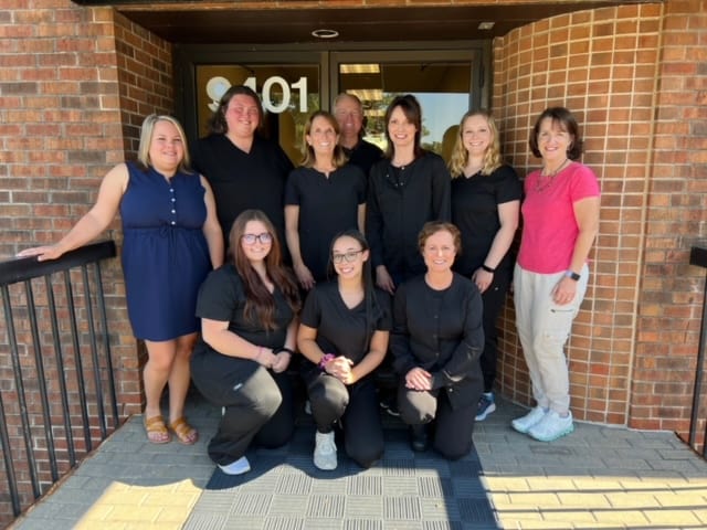 A group of people posing in front of a Restorative Dentistry building.