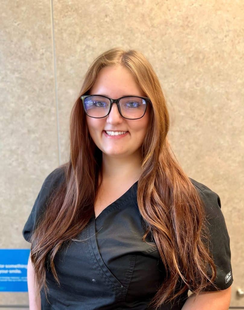 A smiling woman wearing glasses in front of a wall, while posing for an auto draft.