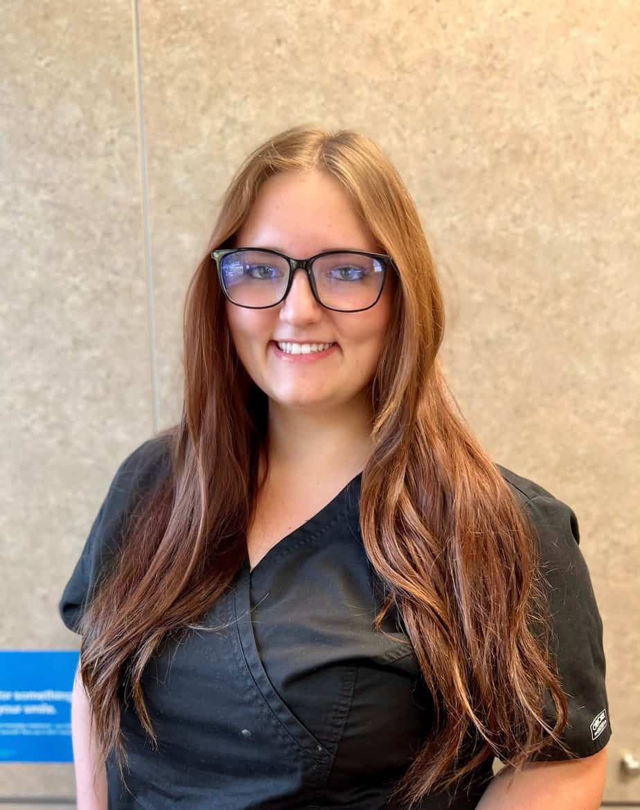 A smiling woman wearing glasses in front of a wall, while posing for an auto draft.