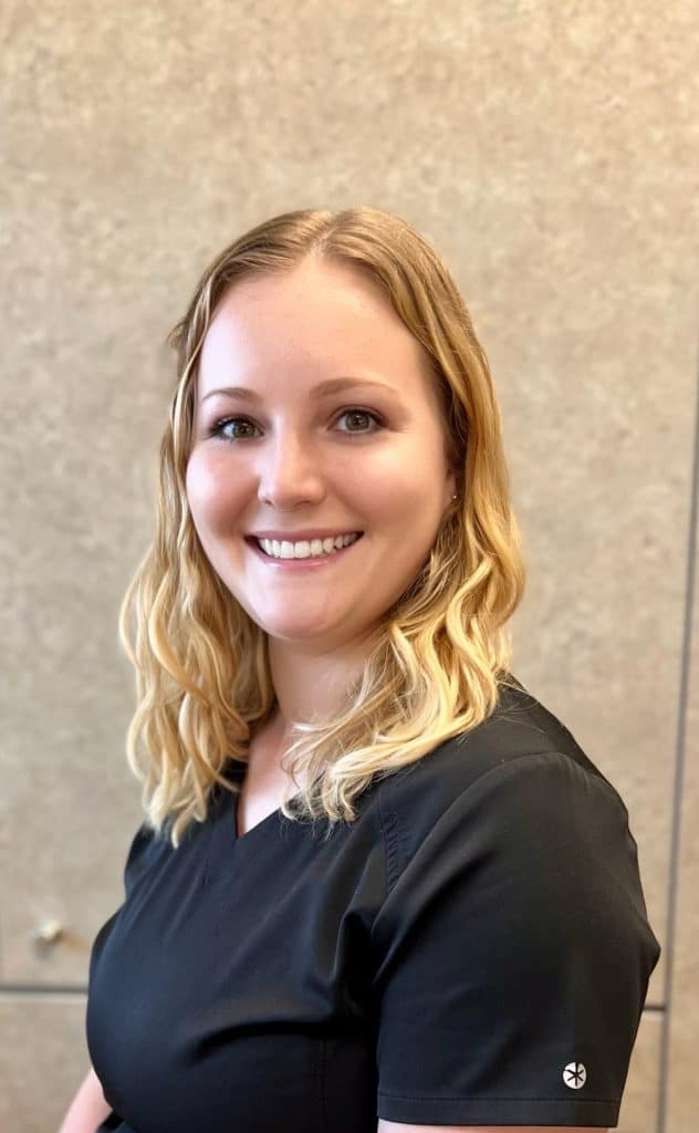 A woman in a black scrub top, radiating a warm smile.