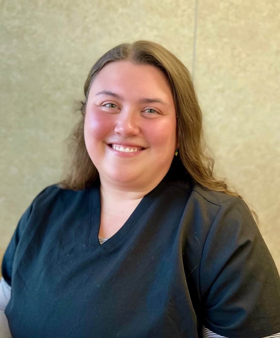 A woman in a black scrub shirt stands with a gentle smile on her face.